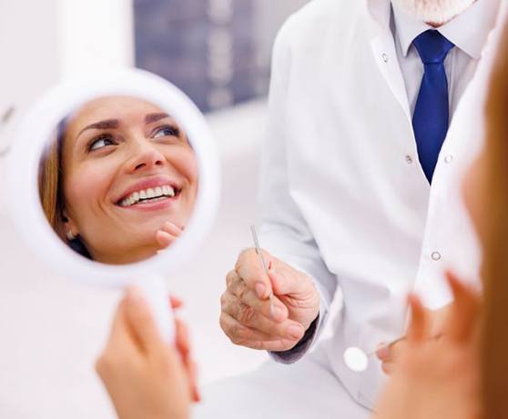 Dental patient holding mirror, smiling at dentist