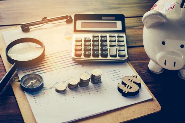 A piggy bank, calculator, and coins sitting next to a clipboard