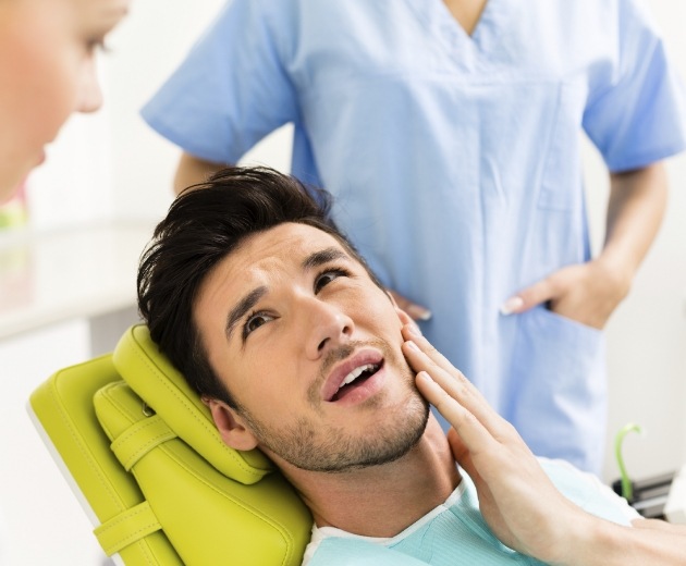 Man holding his jaw in pain while talking to his oral surgeon