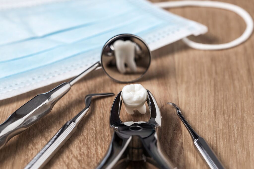 An extracted tooth held by forceps reflected in a dental mirror on a wooden surface